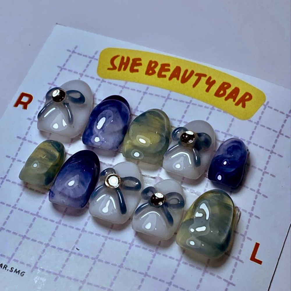 Koleksi eksklusif nail art dari She Beauty Bar di Semarang, memamerkan set kuku pra-desain dengan palet warna biru dan abu-abu serta aksen batu permata yang berkilauan, siap mempercantik tampilan pelanggan dengan gaya yang chic dan personal.